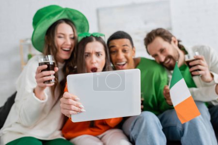Verschwommene interrassische Freunde nutzen digitales Tablet, während sie den Patrick-Tag zu Hause feiern 