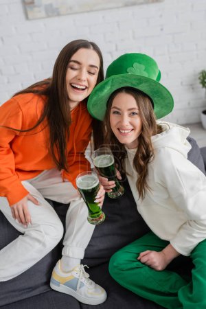Positive young women holding green beer during saint patrick celebration at home 