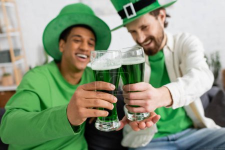 Verschwommene multiethnische Freunde, die während des Patronatsfestes grünes Bier trinken