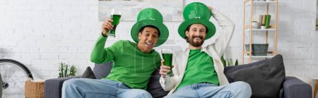 Foto de Felices amigos multiétnicos con cerveza verde mirando a la cámara mientras celebran el día de San Patricio, pancarta - Imagen libre de derechos