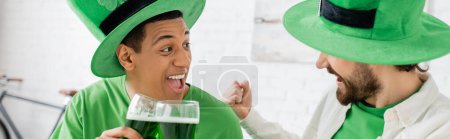 Foto de Excited multiethnic men with green beer celebrating saint patrick day at home, banner - Imagen libre de derechos