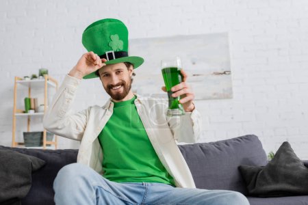 Hombre sonriente en sombrero celebrando el día de San Patricio con cerveza verde en casa 