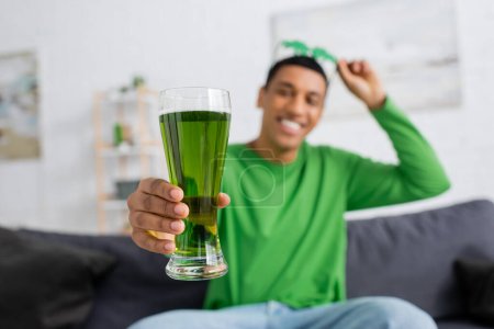 Hombre afroamericano borroso sosteniendo cerveza verde en casa 