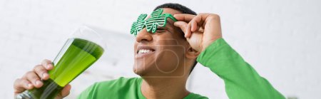 Low angle view of african american man in party sunglasses holding beer at home, banner  mug #639066926