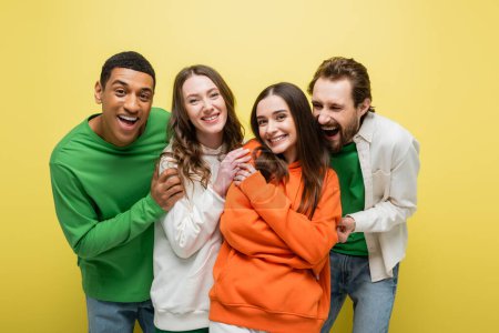 Positive multiethnic friends looking at camera on yellow background 