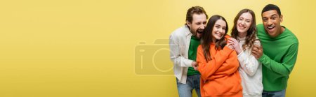 Multiethnic friends in casual clothes looking at camera isolated on yellow, banner 