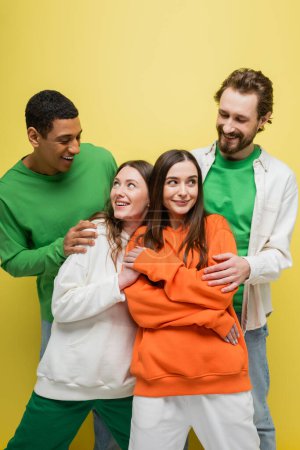 Foto de Positive women looking at interracial friends on yellow background - Imagen libre de derechos
