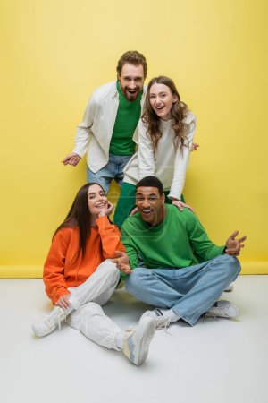 Young interracial friends looking at camera while posing on yellow background 