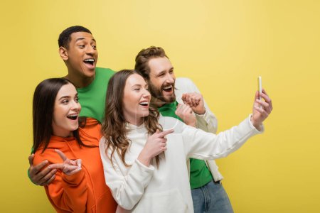 Fröhliche Freunde gestikulieren und nutzen Smartphone isoliert auf gelb 
