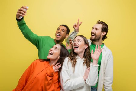 Multiethnic friends having video call on smartphone isolated on yellow 