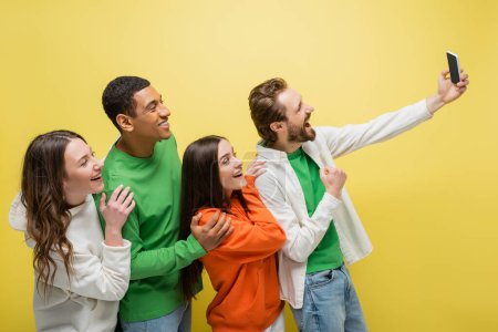 Téléchargez les photos : Homme positif montrant des gestes oui lors d'un appel vidéo près d'amis interraciaux isolés sur jaune - en image libre de droit