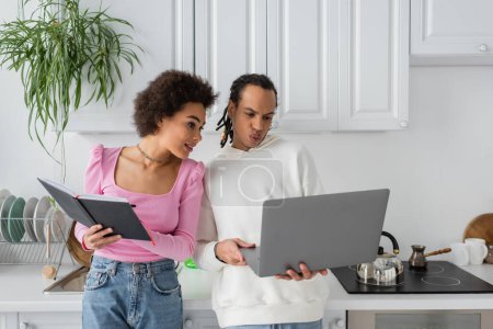 African american couple working with laptop and notebook in kitchen 