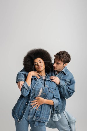 Téléchargez les photos : Man in denim jacket embracing curly african american woman isolated on grey - en image libre de droit
