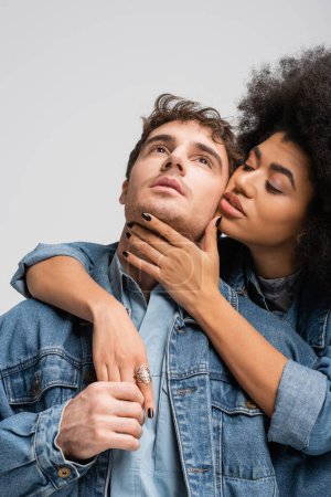 Téléchargez les photos : Curly african american model embracing stylish man in denim clothes isolated on grey - en image libre de droit