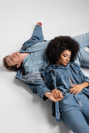 Téléchargez les photos : High angle view of african american woman leaning on man in denim clothes lying on grey - en image libre de droit