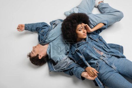 Téléchargez les photos : Top view of stylish african american woman in denim clothes lying with man on grey background - en image libre de droit