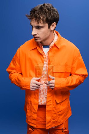 Stylish model in bright orange jacket and shirt isolated on blue 