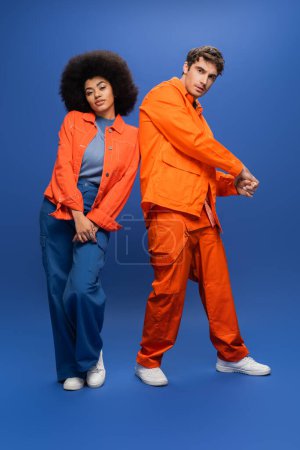 Full length of fashionable interracial models posing on blue background