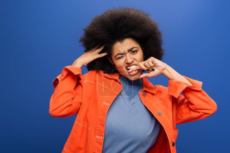 Stylish african american woman winking and biting finger isolated on blue 