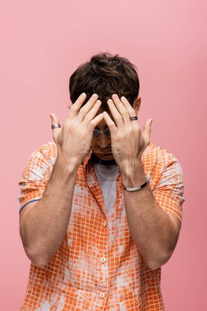 Foto de Trendy brunette man in sunglasses covering face isolated on pink - Imagen libre de derechos