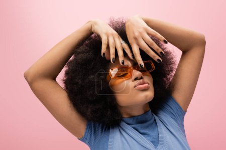 Portrait de femme afro-américaine aux lunettes de soleil boudant les lèvres isolées sur rose 