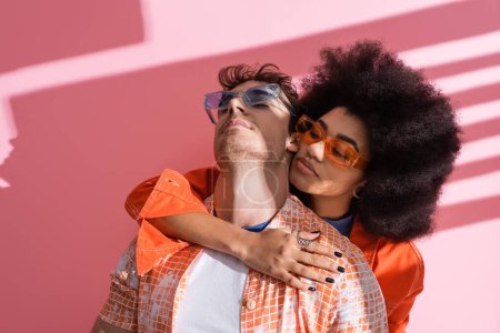 Stylish african american woman hugging man on pink background with shadow 