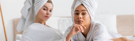 Téléchargez les photos : Jeunes femmes multiethniques en peignoirs blancs et serviettes regardant caméra dans la chambre, bannière - en image libre de droit