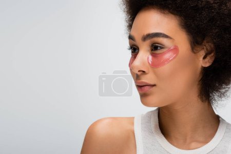 portrait of pretty african american model with lifting eye patches looking away isolated on grey