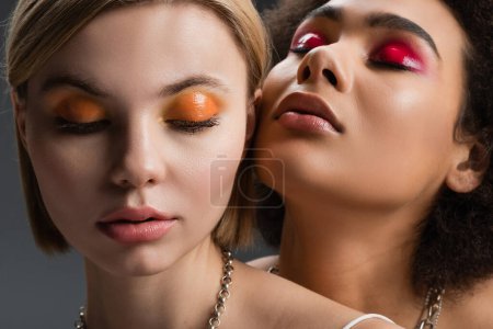 portrait of sensual multiethnic models with bright and glossy eye shadows isolated on grey