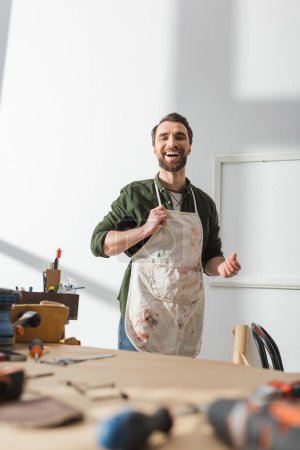 Positive craftsman in dirty apron standing in workshop 