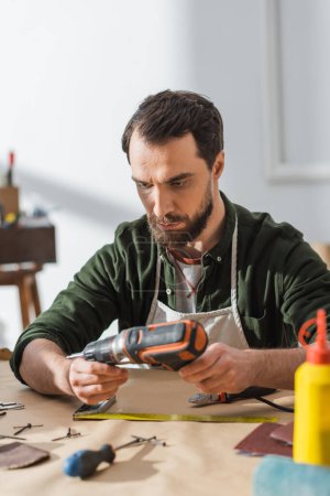 Foto de Bearded craftsman in apron holding electric screwdriver in workshop - Imagen libre de derechos