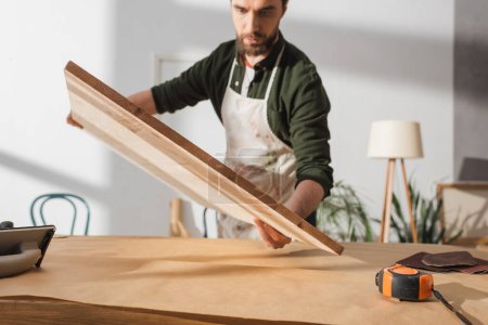Verschwommener Tischler hält Holzbrett neben Tisch in Werkstatt 