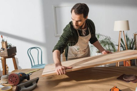 Handwerker legt Holzbrett auf Tisch neben Werkzeug 