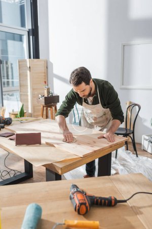 Handwerker mit Schleifpapier auf Holzbrett in Werkstatt 