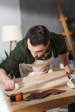 Foto de Bearded craftsman sanding surface of wooden board near ruler on table - Imagen libre de derechos