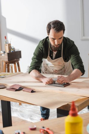 Foto de Craftsman sanding surface of wooden board in workshop - Imagen libre de derechos