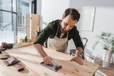 Photo for Workman sanding wooden board near sandpaper in workshop - Royalty Free Image
