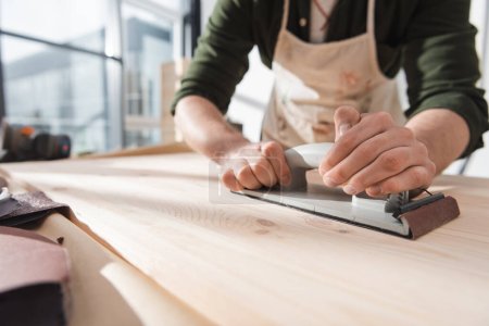 Téléchargez les photos : Cropped view of blurred workman sanding surface of wooden board - en image libre de droit