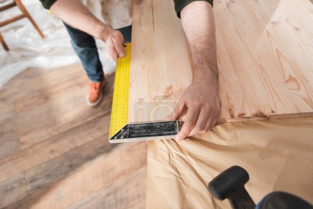 Vue recadrée du charpentier à l'aide d'un outil carré sur une planche en bois 