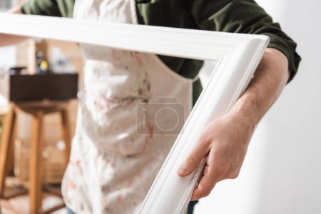 Vue recadrée du restaurateur flou dans le tablier tenant le cadre photo en bois 