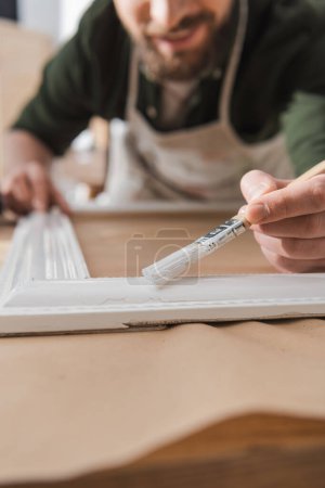 Vista recortada de la pintura borrosa restaurador marco de madera en la mesa 