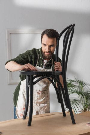 Réparateur barbu dans tablier de ponçage chaise en bois dans l'atelier 