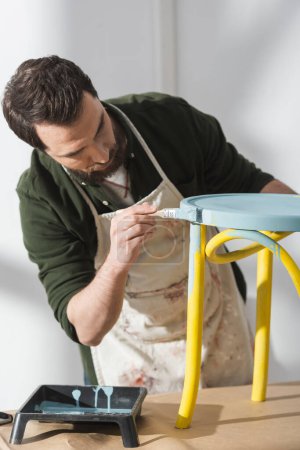 Handwerker malt auf Holzstuhl auf Tisch in Werkstatt 