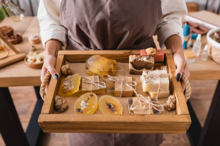 Foto de Wooden tray with assortment of handmade soap in hands of cropped african american craftswoman - Imagen libre de derechos