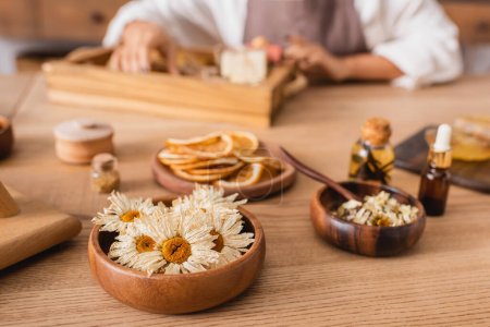 Téléchargez les photos : Selective focus of dried camomiles near essentials oils and african american woman in craft workshop - en image libre de droit