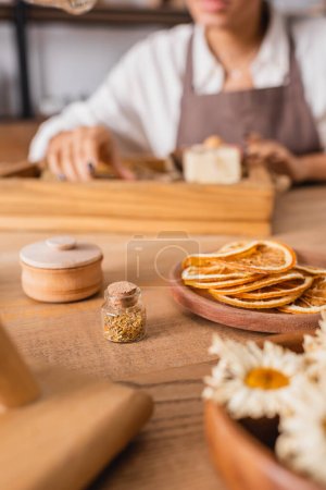 Photo for Cropped view of african american woman near dried orange slices and camomiles on blurred foreground in craft workshop - Royalty Free Image