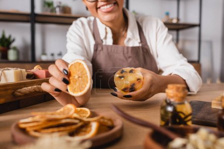 cropped view of african american woman holding dried orange slice and homemade soap in craft workshop