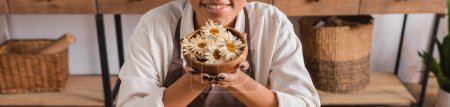Photo for Partial view of happy african american woman holding wooden bowl with dried camomiles in craft workshop, banner - Royalty Free Image
