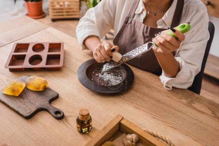 vista recortada del jabón de rejilla de artesana afroamericana cerca del molde de silicona y el aceite esencial en la mesa de madera