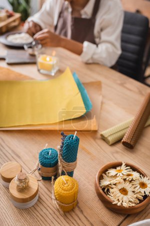 Photo for Dried camomiles and homemade candles near wax sheets and cropped african american craftswoman on blurred background - Royalty Free Image